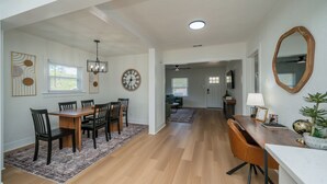 A spacious dining area with a wooden table and chairs, a chandelier, and a clock on the wall. - Charming 2-bedroom house in Kilgore (Kilgore)