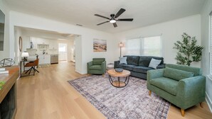A spacious living room with a wooden floor, a green sofa, a round coffee table, and a ceiling fan. - Charming 2-bedroom house in Kilgore (Kilgore)