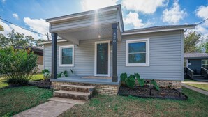 A two-story house with a front porch, a brick foundation, and a small garden area. - Charming 2-bedroom house in Kilgore (Kilgore)