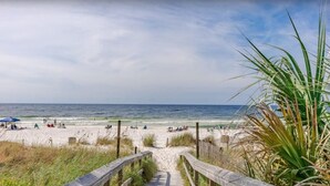 En strand med en träpromenad som leder ner till stranden, sandstrand och utsikt över havet.