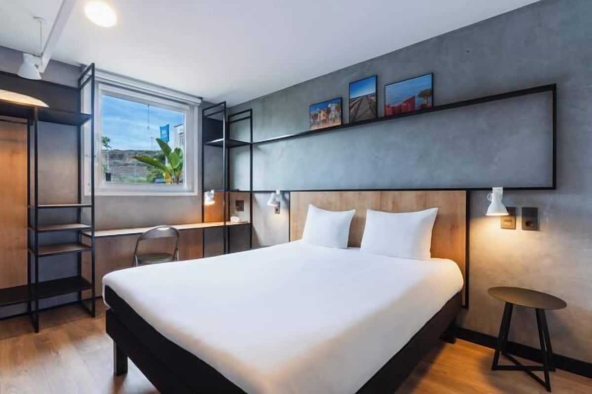 Ein modernes Hotelzimmer mit einem großen Bett, einem Schreibtisch, einem Sessel und einem Fenster mit Blick.
