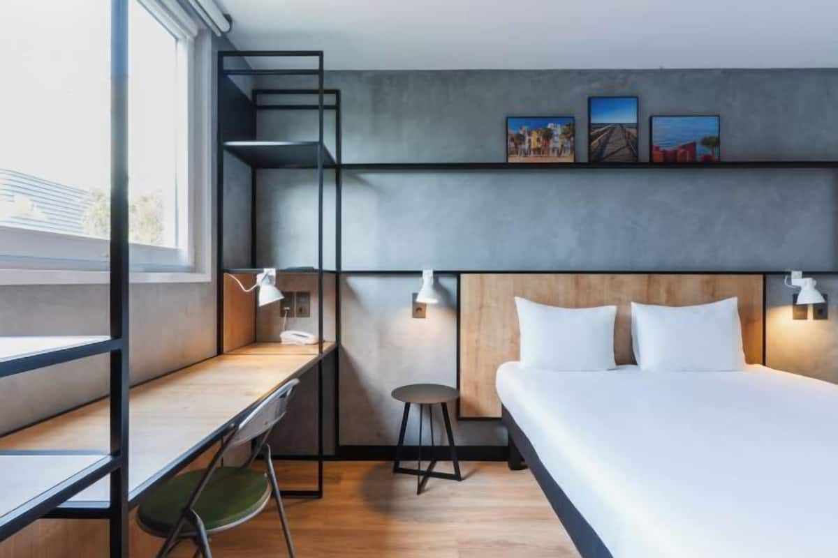 Ein modernes Hotelzimmer mit Bett, Schreibtisch, Stuhl und Blick ins Freie.