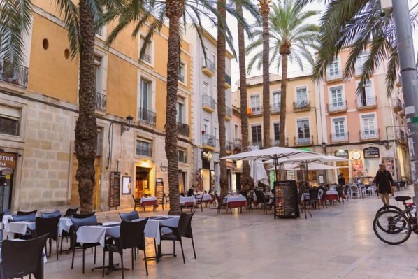 An outdoor café area with tables and chairs, surrounded by palm trees and buildings. - Ibis Hotel Alicante (Alicante)