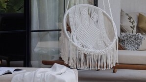 Makramee-tekniikalla valmistettu riipputuoli huoneessa, jossa on suuri ikkuna, sohva ja koristeellinen seinävaate.
