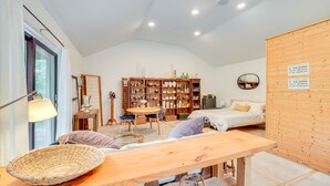 A cozy room with a wooden table, wicker basket, and a bookshelf filled with decorative items. - 1850s Barn Studio on 4.5 Hudson Valley Acres! (Highland)