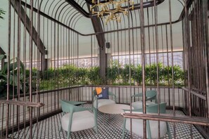 A cozy indoor seating area with a curved ceiling and metal railings, featuring a round table and cushioned chairs. - Paxtonz Leisure Suites Kuala Lumpur (Petaling Jaya)