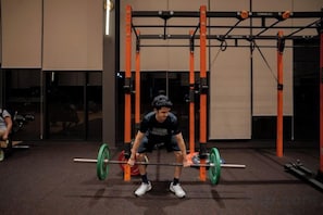 Une personne effectue un exercice de squat avec une barre chargée dans une salle de sport dont l’équipement est de couleur orange.