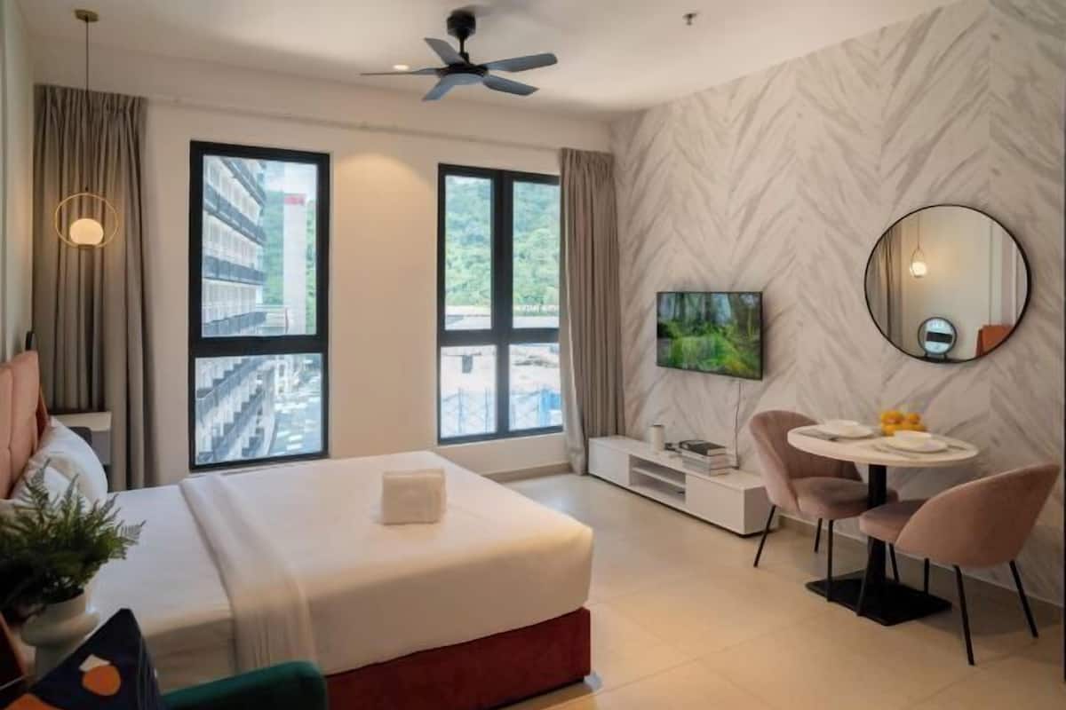 Une chambre d’hôtel moderne équipée d’un lit, d’une télévision, d’un coin repas avec des chaises et de grandes fenêtres.
