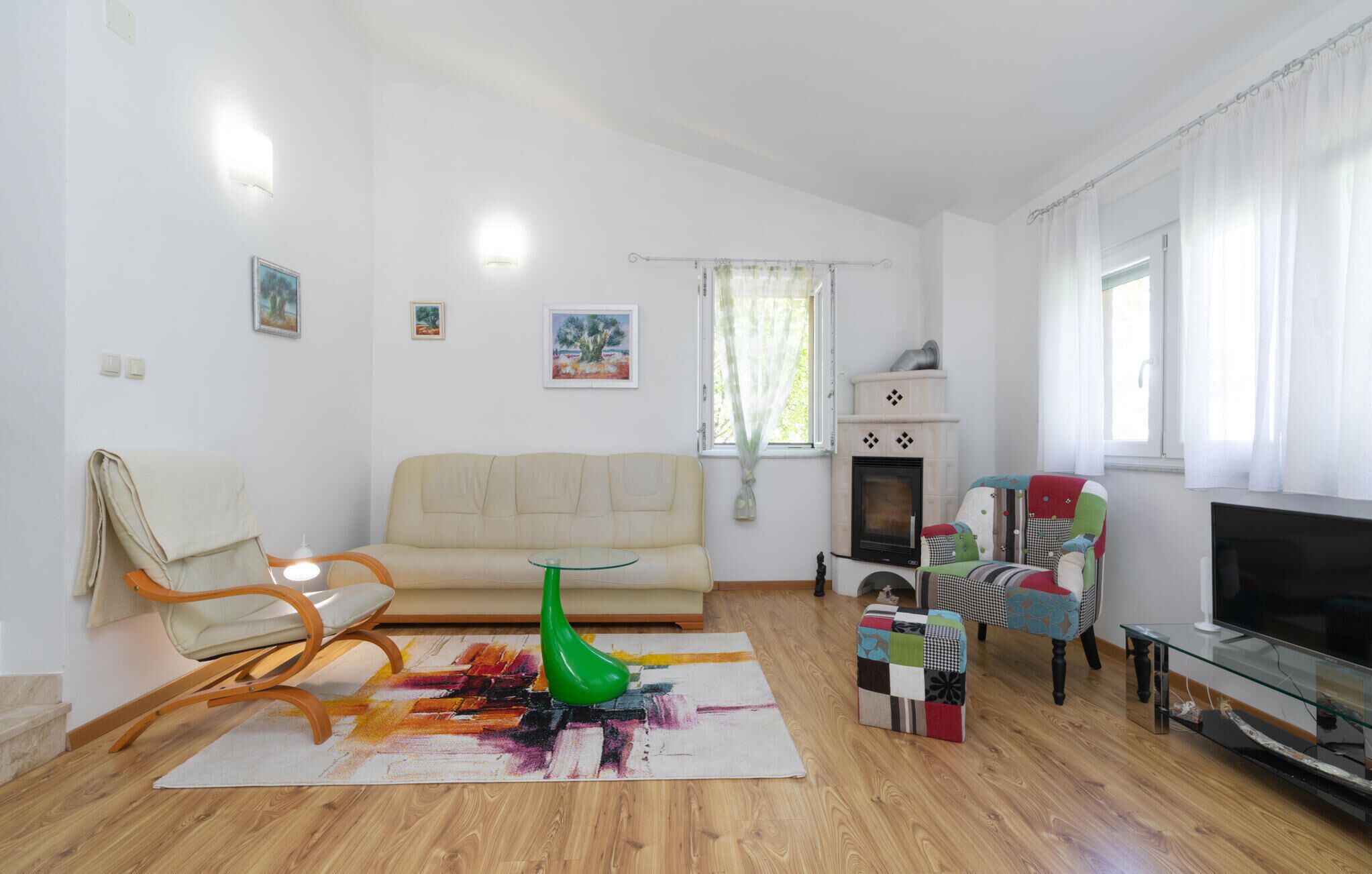 Una sala de estar con un sofá, un jarrón verde, un tapete colorido, un televisor y una chimenea.