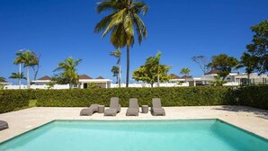 Ein Swimmingpool mit Liegestühlen und Palmen, umgeben von Gebäuden unter blauem Himmel.