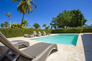 Ein Swimmingpool mit Liegestühlen, Palmen und einer Hecke.