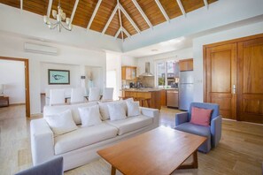 A spacious living area with a sofa, a coffee table, and a chair. There is a kitchen in the background with wooden cabinets and a refrigerator. - Modern 3BR Villa-Private Pool -Sosúa Ocean Village (Sosúa)