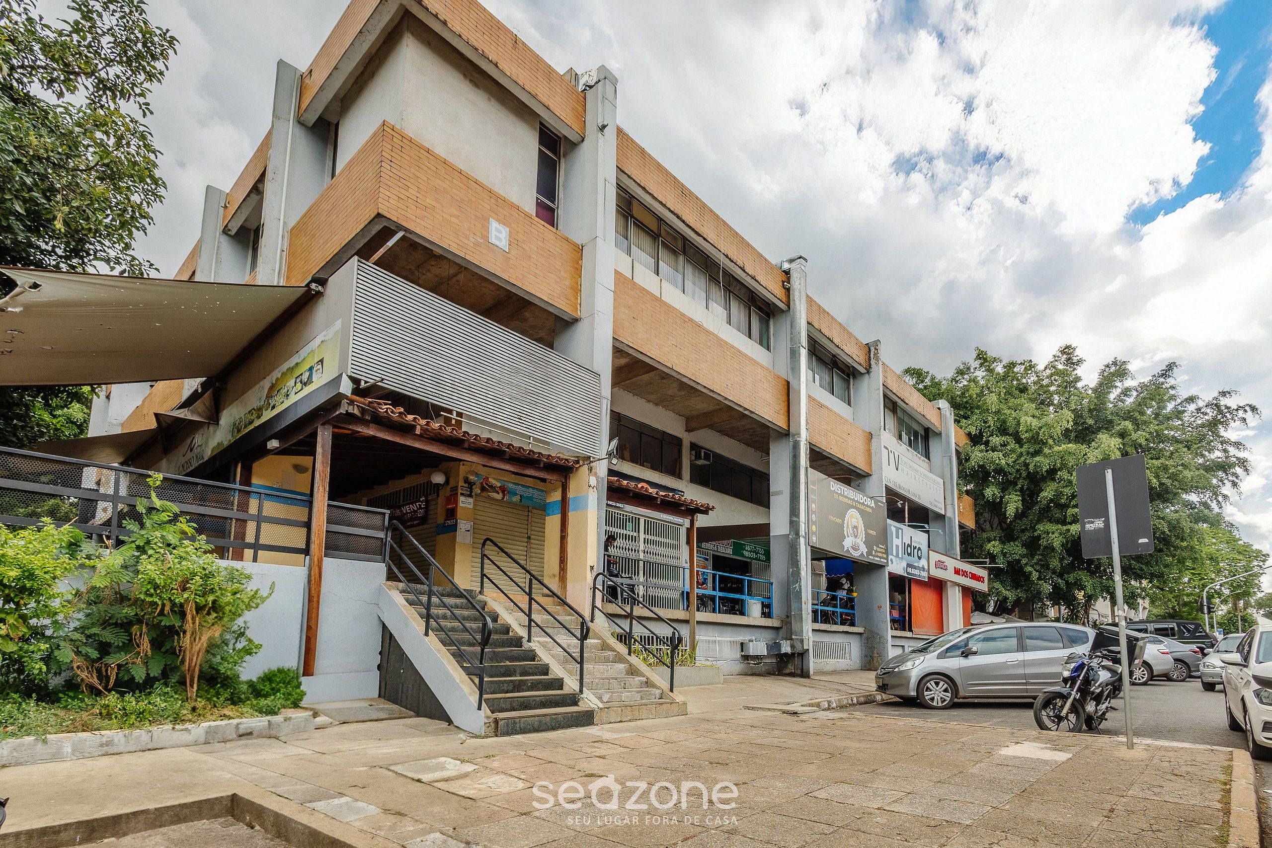 Un edificio de varios pisos con una escalera que conduce a la entrada, una motocicleta estacionada y un coche en la calle.