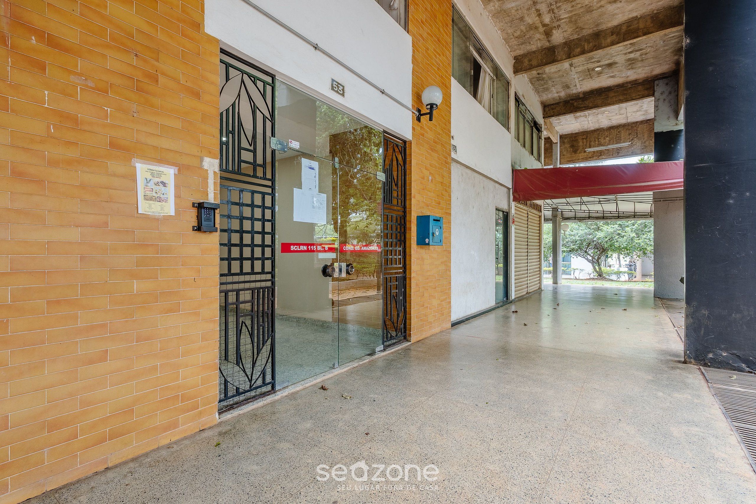 A corridor with a brick wall, a glass door with a metal gate, and a red awning.