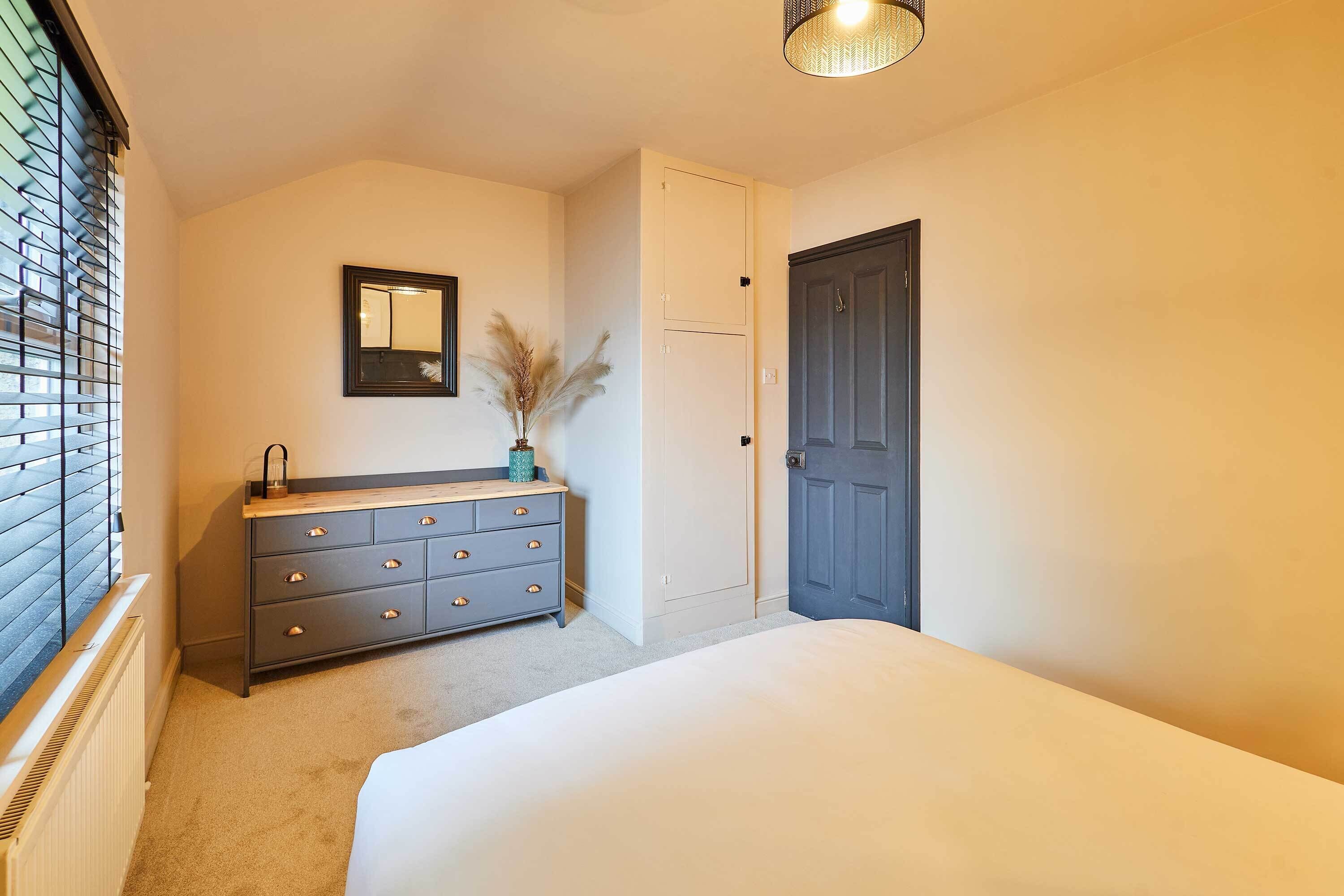A bedroom with a bed, a dresser, a mirror, a door, and a radiator.