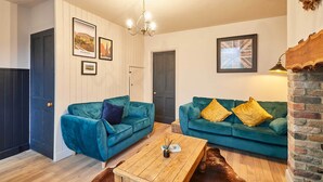 A living room with two teal sofas, a wooden coffee table, and a brick fireplace. - Host Stay Daisy Cottage (Ripon)