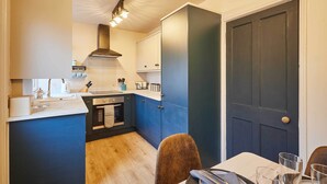 A compact kitchen with a central island, a dining area with a table and chairs, and a dark door. - Host Stay Daisy Cottage (Ripon)