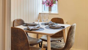A dining table set with plates, cutlery, and glasses, surrounded by upholstered chairs. - Host Stay Daisy Cottage (Ripon)