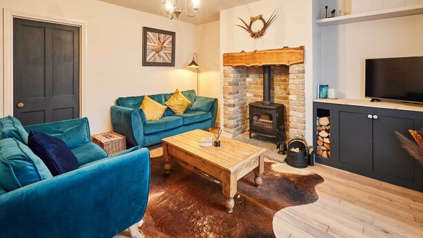 A cozy living room with a blue sofa, a wooden coffee table, a stone fireplace, and a television on a cabinet. - Host Stay Daisy Cottage (Ripon)