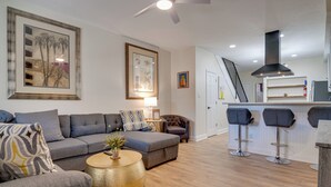 A modern living room with a grey sofa, a round coffee table, and a staircase leading to a kitchen area with bar stools. - 3 Mi to Dtwn Indy: Urban Retreat w/ Outdoor Space (Indianapolis)