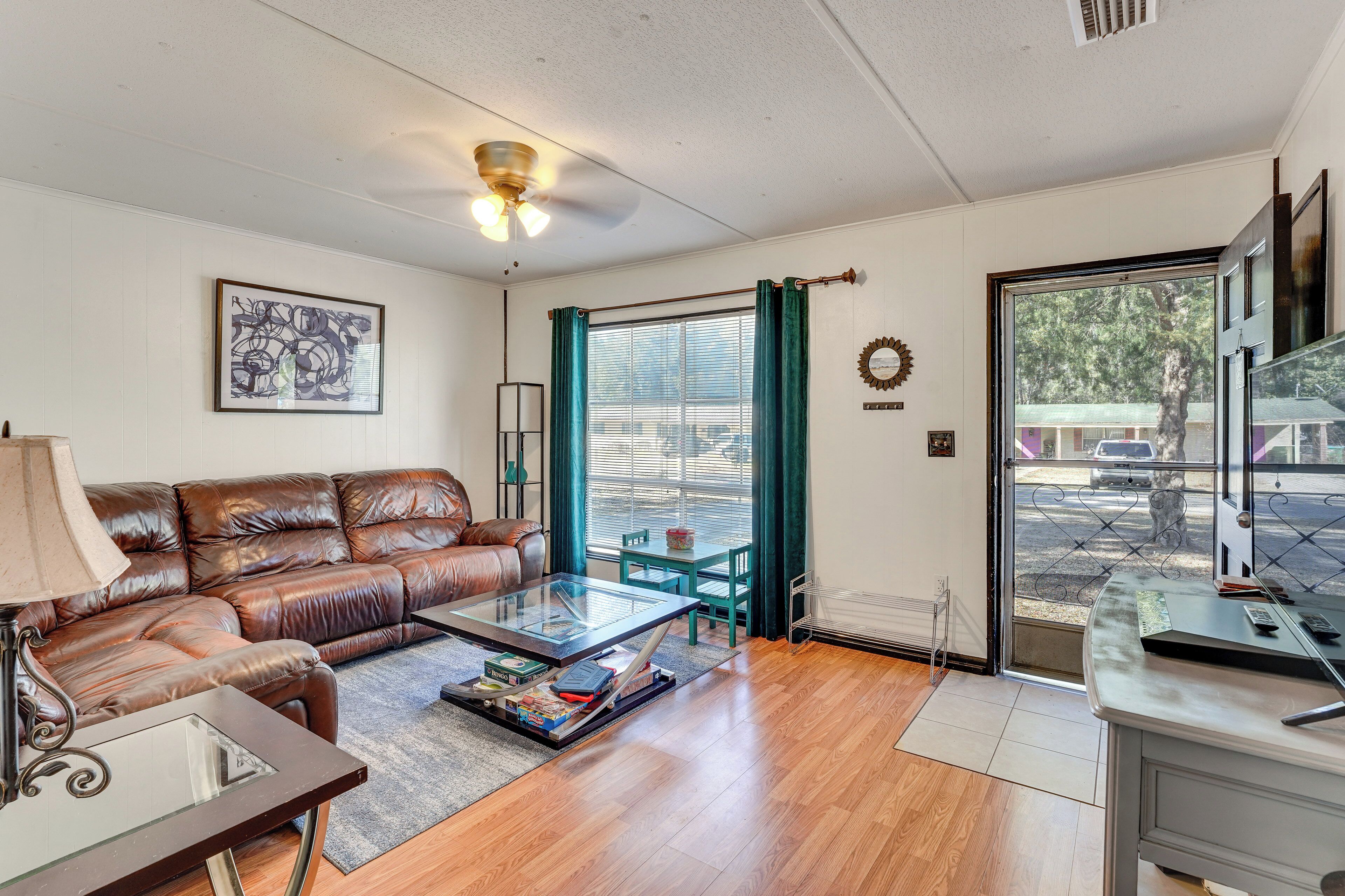 A living room with a leather sofa, a glass coffee table, a desk, and a view through a glass door.