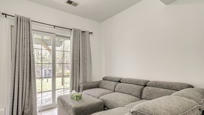 A modern living room with a sectional sofa, a small ottoman, and a window with curtains.