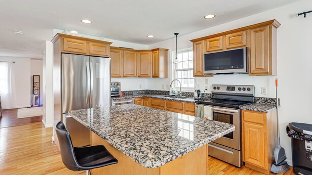 A modern kitchen with granite countertops, stainless steel appliances, wooden cabinets, and a large island.