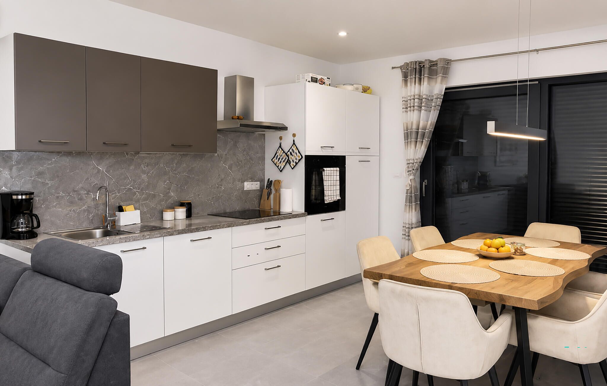 Een moderne keuken met witte kasten, een zwarte kookplaat en een eethoek met een houten tafel en stoelen.