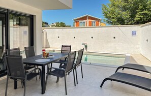 Une terrasse avec une table et des chaises, une piscine et un bâtiment en arrière-plan.