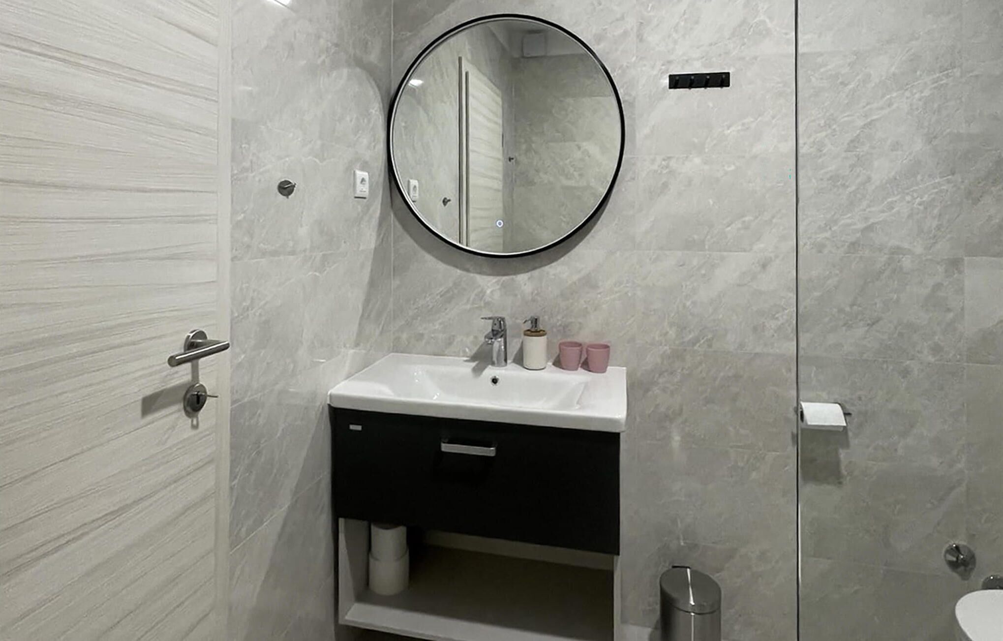 Ein modernes Badezimmer mit einem weißen Waschbecken, einer schwarzen Kommode und einem runden Spiegel.