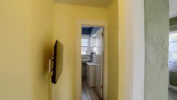 A narrow hallway with a door leading to a bathroom with a sink and mirror.