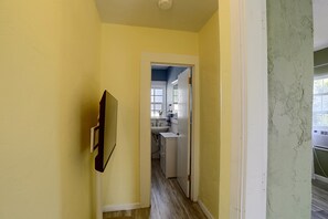 Un pasillo estrecho con una puerta que da a un baño con lavamanos y espejo.