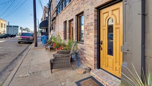 A brick building with a yellow door, a wicker chair, and a potted plant on the sidewalk. - Convenient Couple's Retreat in Dtwn Marshall! (Marshall)