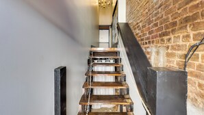 A staircase with wooden steps and metal chains, leading to a room with a brick wall and a chandelier. - Convenient Couple's Retreat in Dtwn Marshall! (Marshall)