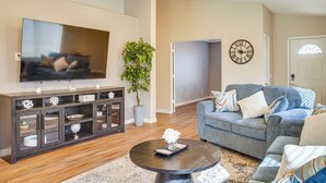 A living room with a dark wood cabinet, a grey sofa, a round coffee table, and a large flat-screen TV. - 2 Mi to Surprise Stadium! Snowbird Haven w/ Pool (Surprise)