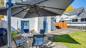 An outdoor patio with a table and chairs, a covered umbrella, and a white RV in the background. - Pet-Friendly Susanville Home w/ Pickleball Court (Susanville)