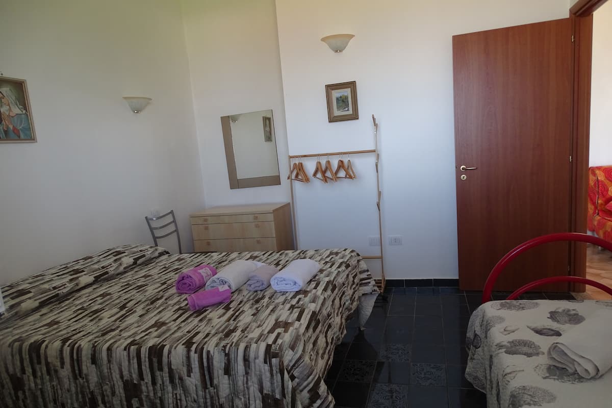 A bedroom with a bed, a dresser, a chair, a wardrobe, and a door.