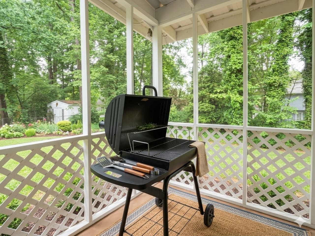 A covered outdoor area with a grill, a table with utensils, and a lattice railing.
