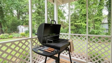 A covered outdoor area with a grill, a table with utensils, and a lattice railing.