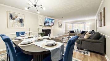 A dining area with a round table set for four, a gray sofa, and a flat-screen TV mounted on the wall.