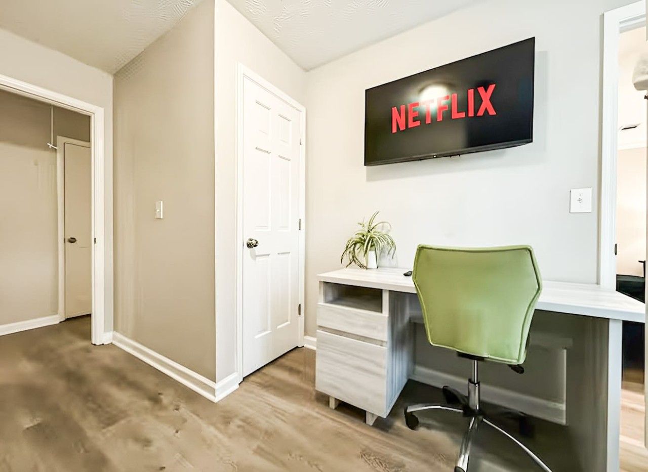 A room with a desk, a chair, a television mounted on the wall, and a door.