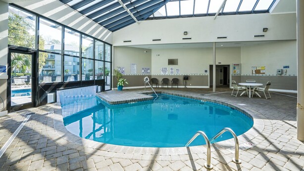 Une piscine intérieure dotée d’une verrière, un espace aménagé au bord de la piscine avec des chaises, et une vue sur l’extérieur.