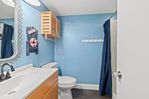 Une salle de bain avec un lavabo blanc, des toilettes, un miroir et un rideau de douche.