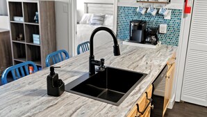 Une cuisine moderne avec un évier noir, une machine à café et un dosseret de carrelage bleu.