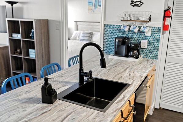 A modern kitchen with a black sink, a coffee machine, and a blue tiled backsplash.