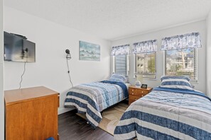 Une chambre avec deux lits, une commode en bois, un téléviseur à écran plat fixé au mur et un tableau accroché au mur.