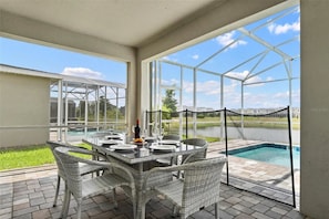 A covered patio with a table set for dining, overlooking a swimming pool and a view of a residential area. - Family 9BR Lakeview Home w/ Pool, Jacuzzi & Game Room on ChampionsGate Resort! (Kissimmee)