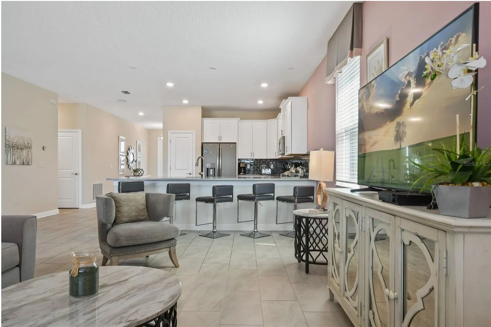 A modern kitchen with white cabinets, a central island with bar stools, and a dining area with a marble table and chairs.