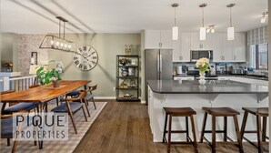 Een moderne keuken met een centraal eiland, hanglampen en een klok aan de muur.