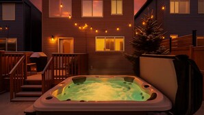 Een bubbelbad in een achtertuin met een houten terras en een trap naar een huis.